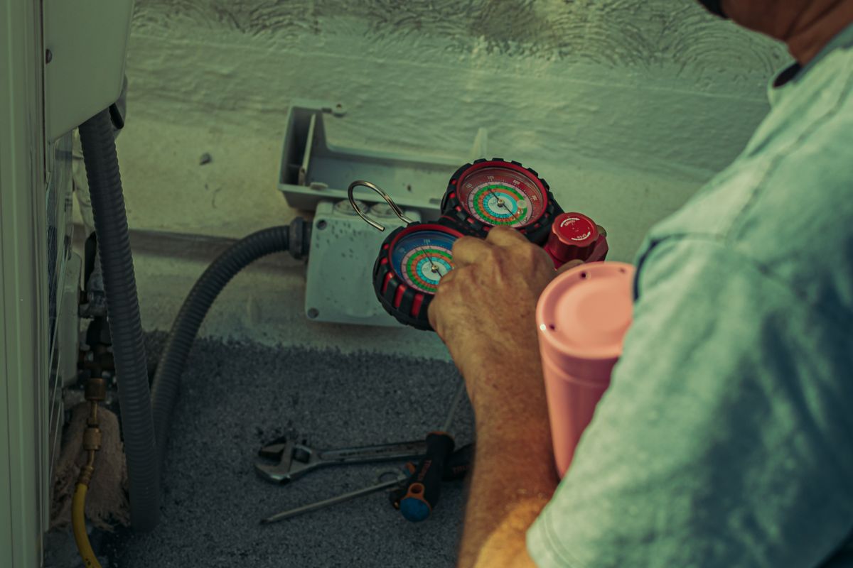 HVAC technician checking an outdoor air conditioning unit with service gauges connected.